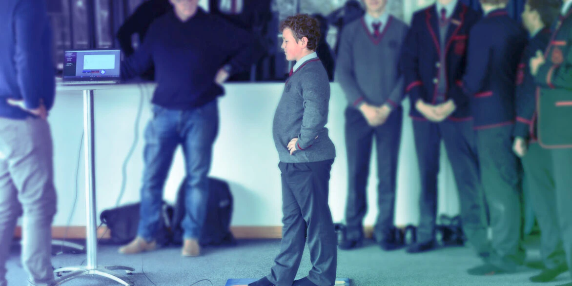 Child performing balance assessment on mat while supervised by instructor with monitoring equipment