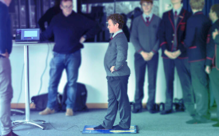 Child performing balance assessment on mat while supervised by instructor with monitoring equipment